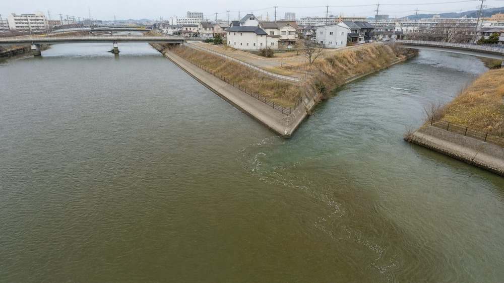二つの都市河川が合流して水色の境界と渦が生まれる地点