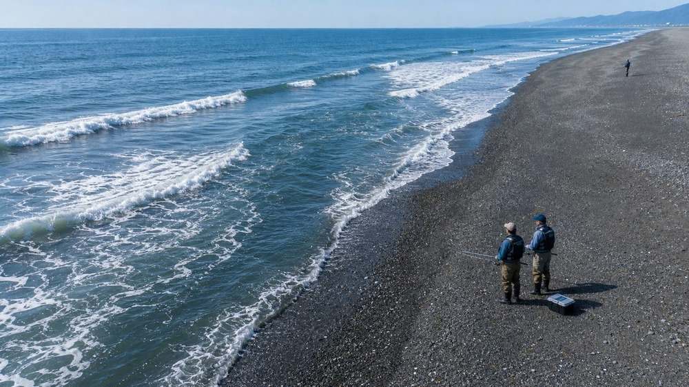 離岸流の水面パターンを乾いた砂利浜から確認する釣り人